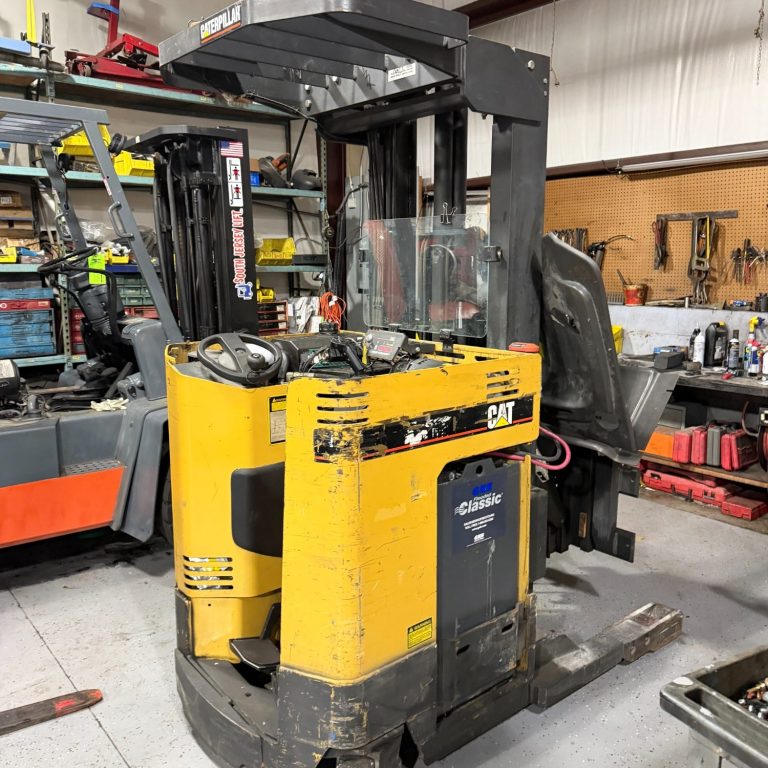 Weekly Forklift Rental Photo Yellow forklift with a clear cabin, parked in a workshop filled with tools and equipment.