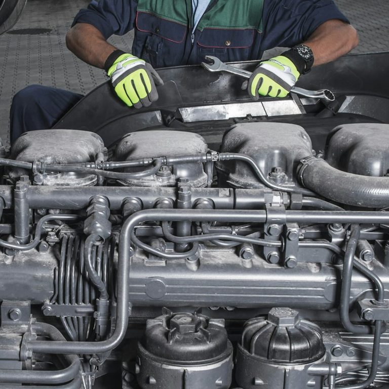A South Jersey Lift Technician on the job! Mechanic repairing a large engine, wearing gloves and work attire, in a workshop setting.