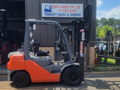 TOYOTA 8FGU25 Orange forklift parked outside a warehouse with a business sign above.